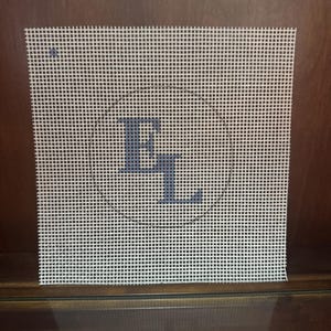 Könnte beinhalten: Quadratische Leinwand mit Gittermuster, mit einem dunkelblauen Buchstaben "R" und einem Teil des Buchstabens "L". Die Leinwand ist weiß mit einem Gitter aus kleinen schwarzen Quadraten. Die Buchstaben sind stilisiert und scheinen handgezeichnet zu sein.