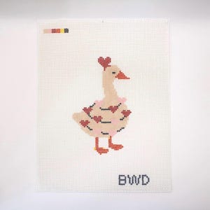 May include: Needlepoint canvas featuring a goose design. The goose is light tan with red heart accents on its body and a heart on its head. It has a pink ruffle around its neck and red feet. The letters "BWD" are at the bottom.