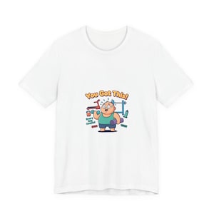 May include: White t-shirt featuring a cartoon illustration of a person lifting weights. The design includes the text "You Got This!" and other fitness-related graphics. The person is wearing a teal top and holding a purple yoga mat.