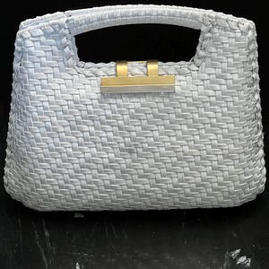 May include: A light gray woven handbag with a rectangular shape and a top handle. The bag features a gold-colored clasp and a woven pattern throughout. The handbag is designed for carrying essentials.