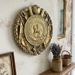 Op de afbeelding: Een ronde goudkleurige wandplaat met een centraal reliëf van een persoon te paard, omringd door de tekst Confederate States of America en Deo Vindice. Het ontwerp bevat gekruiste vlaggen, lauwerkransen en een schild met het jaartal 1862.
