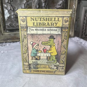 May include: A rectangular box set titled Nutshell Library by Maurice Sendak. The cover features a yellow and beige illustration of a child in a winter hat and a green alligator in a yellow jacket sitting at a table, with a cat and mouse below.