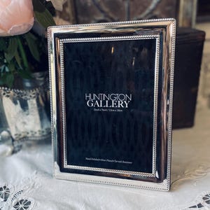 May include: A rectangular silver-plated photo frame with a beaded border. The frame has the text "HUNTINGTON GALLERY" and measurements of 5 inches x 7 inches / 13cm x 18cm. The frame is hand polished and tarnish resistant.