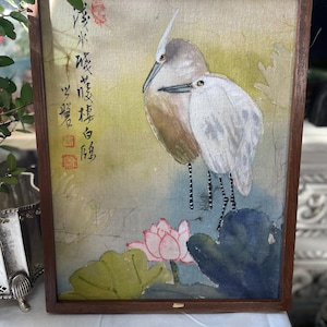 May include: A framed watercolor painting featuring two birds with long beaks and legs, set against a backdrop of a lotus flower and leaves. The artwork is in a wooden frame and includes Asian calligraphy.