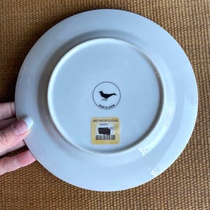 May include: White ceramic plate with a bird logo and the text "MADE IN JAPAN". The plate has a sticker that says "ANTHROPOLOGIE" and a price tag.