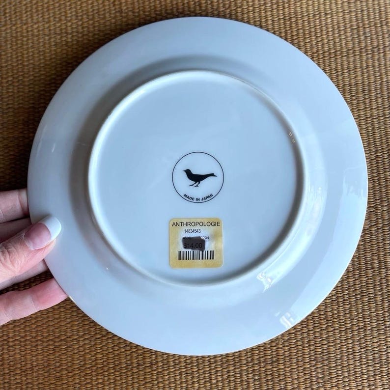 May include: White ceramic plate with a bird logo and the text "MADE IN JAPAN". The plate has a sticker that says "ANTHROPOLOGIE" and a price tag.