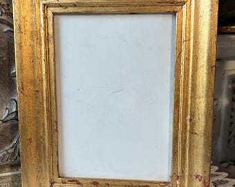 Può includere: Una cornice rettangolare con una finitura dorata anticata caratterizzata da sottotoni rossi visibili e una consistenza usurata. La cornice racchiude un inserto bianco semplice che mostra al centro un leggero schizzo a matita di un diamante.