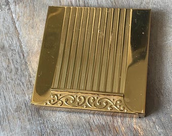 Polvos compactos cuadrados vintage dorados de AVON con cierre de pestillo y diseño ornamental.
