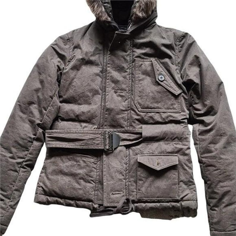 May include: A dark gray winter jacket with a faux fur-lined hood. The jacket features a belted waist, multiple pockets, and a button-up front. The jacket has a quilted design and a drawstring at the bottom.