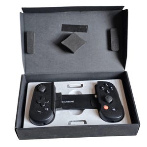 May include: A black mobile gaming controller with the word BACKBONE printed in white on the center bridge. The device features a directional pad, two analog sticks, action buttons labeled A, B, X, Y, and an orange button, all housed in a black box.