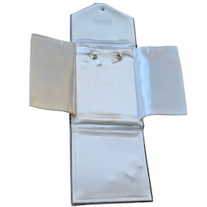 May include: Open gray jewelry case with a white satin interior. The case is rectangular with a flap closure and the words "Bergdorf Goodman" printed on the inside flap. The case is designed to hold jewelry.