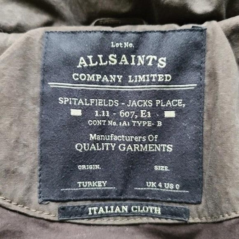 May include: Close-up of a dark navy label from AllSaints Company Limited. The label includes text such as "Spitalfields - Jacks Place" and "Italian Cloth". The label also indicates the origin is Turkey and the size is UK 4 US 0.