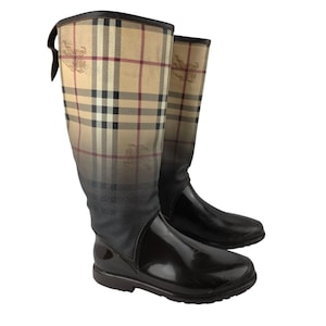 May include: A pair of tall, knee-high rain boots. The upper portion features a beige, brown, and red plaid pattern, while the lower part is a glossy dark brown. The boots have a pull tab at the top and a rounded toe.
