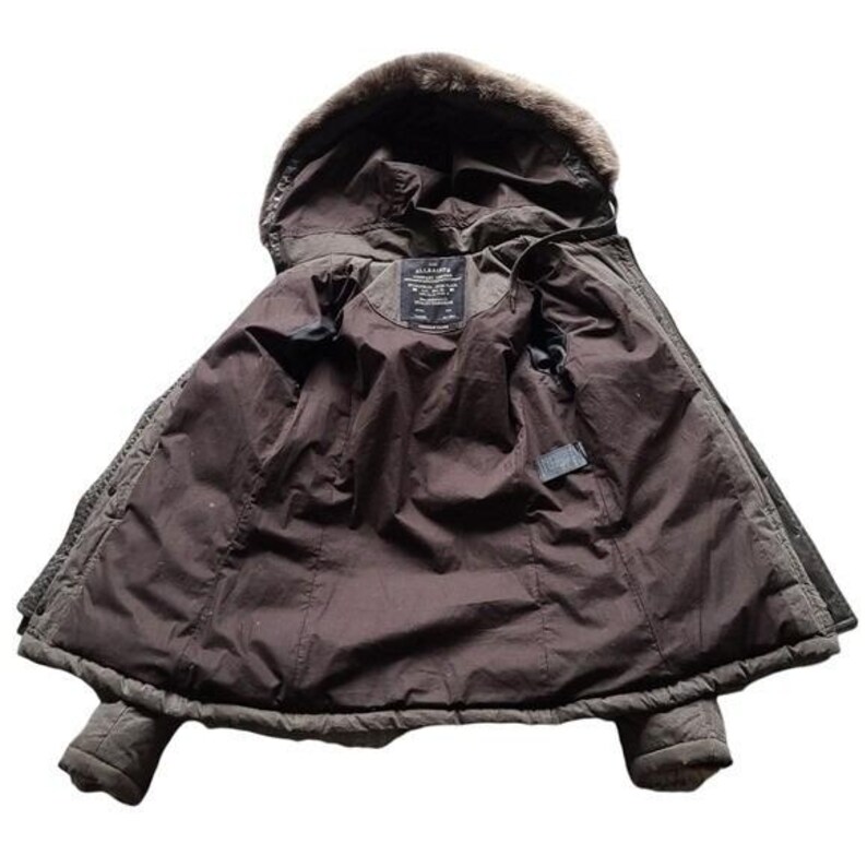 May include: A brown winter coat with a faux fur-lined hood. The coat is open, revealing a dark brown interior lining and a label near the collar. The coat has a quilted design and two pockets.