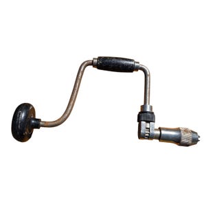 May include: An antique hand drill with a black handle and knob. The drill is made of metal with a curved design and a chuck for holding drill bits. The tool is designed for manual operation.