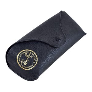 Puede incluir: Estuche de gafas de sol de cuero negro con cierre de bot&oacute;n a presi&oacute;n. El estuche presenta un emblema dorado con las palabras "Ray-Ban Sunglasses by Luxottica" y "100% UV protection". Dise&ntilde;ado para proteger gafas.