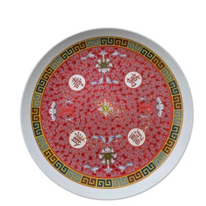 May include: Circular ceramic plate with a white edge and a red central design. The pattern includes Chinese characters, floral motifs, and a geometric border in blue, yellow, and black.