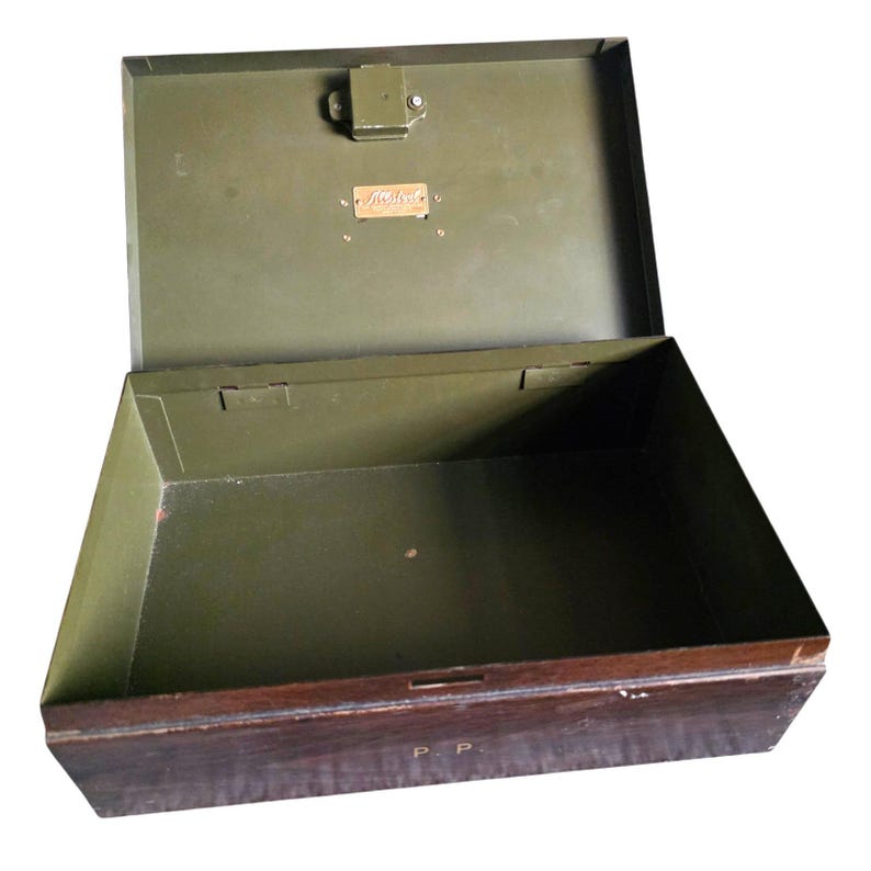 Pode incluir: Uma caixa de metal vintage aberta, com interior e tampa verde-oliva escuro. O exterior &eacute; castanho escuro com uma moldura castanha mais clara. Uma pequena placa de metal &eacute; fixada no interior da tampa. A caixa est&aacute; vazia.