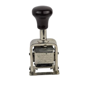 May include: A vintage Roberts Model 49 numbering machine. The device has a black handle and a silver-colored metal frame. The text "ROBERTS NUMBERING MACHINE CO BROOKLYN, N.Y. LONDON & MANCHESTER ENGLAND PAT'D U.S. & EUROPE MODEL 49" is visible.
