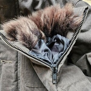 May include: Close-up of a brown winter coat with a faux fur collar. The coat has a zipper closure and a dark blue satin lining. The coat is made of a durable, textured fabric.