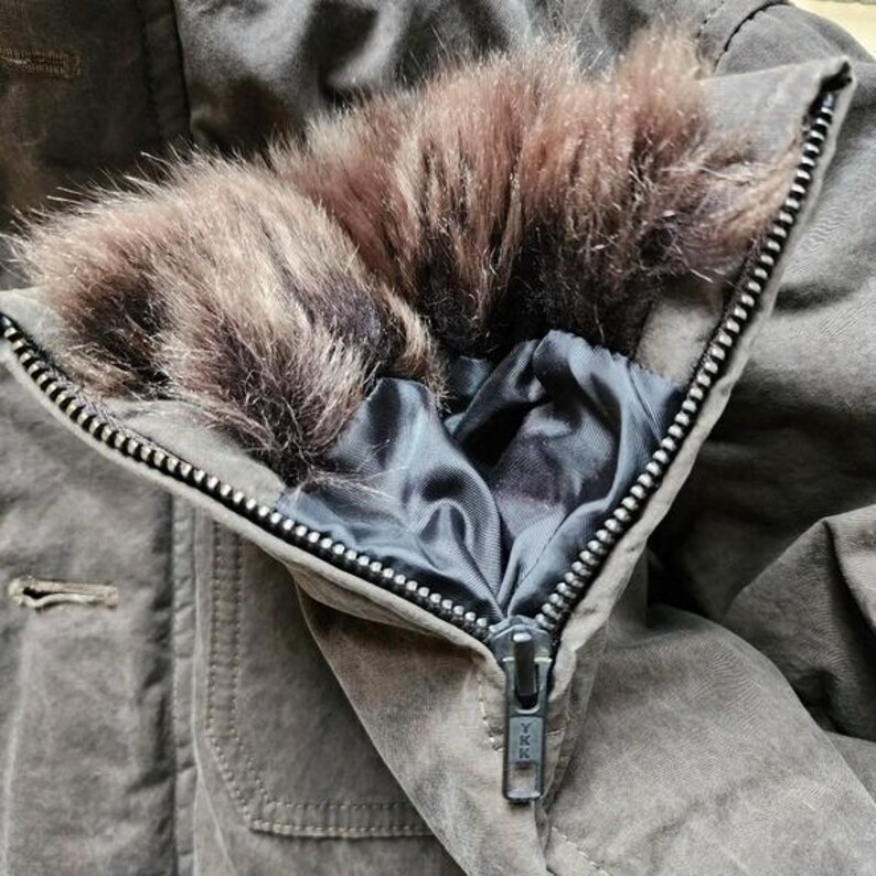 May include: Close-up of a brown winter coat with a faux fur collar. The coat has a zipper closure and a dark blue satin lining. The coat is made of a durable, textured fabric.