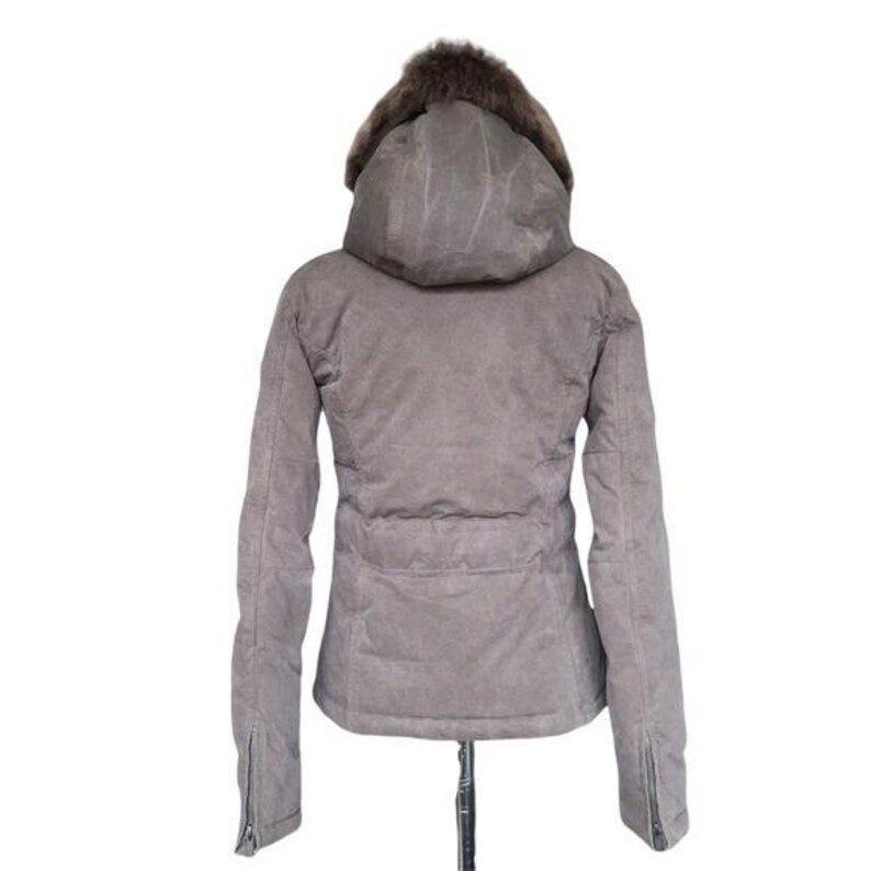 May include: A gray winter jacket with a hood and fur trim. The jacket has a zipper closure on the sleeves and a cinched waist. The hood is lined with brown fur.