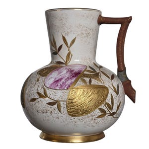 May include: A ceramic pitcher with a speckled white finish, featuring a brown handle and gold-toned base. The body is decorated with gold leaf-like patterns, a purple oval landscape illustration, and a textured gold seashell-shaped relief.