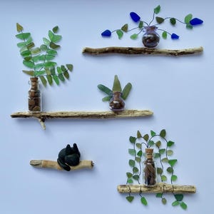 May include: A decorative arrangement featuring small glass bottles on driftwood shelves. The bottles contain natural elements and are adorned with green and blue glass pieces. A black cat figurine is also included in the display.