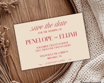Puede incluir: Una invitación de boda color crema con texto rojo que dice "save the date" y detalles de la boda de Penélope y Elías. La invitación está sobre una bandeja de madera con plantas secas y una manta de punto.