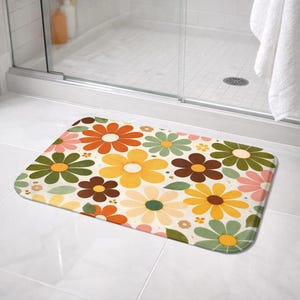 Könnte beinhalten: Eine rechteckige Badematte mit einem Retro-Blumenmuster. Die Matte zeigt große Blumen in Orange-, Gelb-, Braun-, Grün- und Rosatönen auf cremefarbenem Hintergrund. Für den Einsatz im Badezimmer konzipiert.