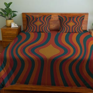 以下が含まれることがあります： 木製のヘッドボードとナイトスタンドを備えたベッド。ベッドには、赤、オレンジ、ティール、ゴールドの色合いのレトロな波模様の掛け布団カバーと枕カバーが2つ付いています。ベッドは作られています。