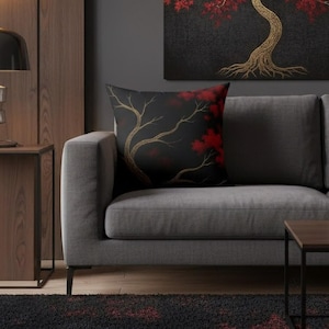 May include: Black throw pillow with a gold tree branch design and red leaves. The pillow is on a gray sofa, with a matching painting in the background. The room has a modern, minimalist aesthetic.