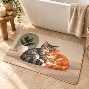 Op de afbeelding: Een rechthoekige badmat met een geometrische illustratie van twee slapende katten, een grijze en een oranje, die tegen elkaar aan liggen. Het ontwerp bevat een gestileerde kamerplant op de achtergrond in een lichtbeige, zandkleurig palet.