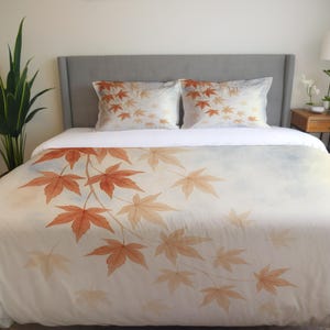 May include: A white duvet cover and two pillowcases featuring a watercolor design of orange and tan maple leaves. The leaves are arranged on a white background with a soft, blue and white gradient.