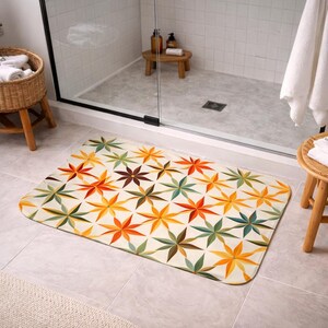 Peut inclure: Un tapis de bain rectangulaire avec un motif floral répété en nuances d'orange, de jaune, de vert et de marron sur un fond crème. Le tapis est posé sur un sol carrelé devant une douche.