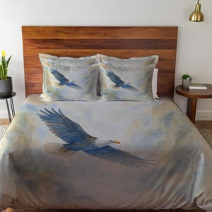 Könnte beinhalten: Bettwäsche-Set mit einem Aquarellgemälde eines Weißkopfseeadlers im Flug. Der Bettbezug und die beiden Kissenbezüge zeigen den Adler mit blauen und weißen Federn vor einem bewölkten Himmel. Die Bettwäsche hat eine neutrale Farbpalette.