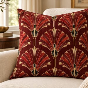 May include: A square throw pillow featuring a deep red velvet fabric with a repeating fan-shaped pattern in gold and black. The geometric design consists of radiating lines that form stylized fan motifs across the entire surface of the pillow.