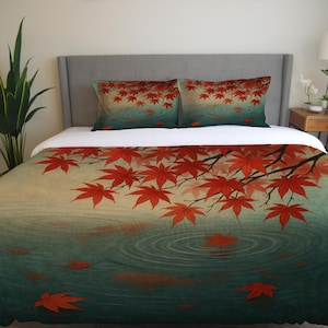 May include: A duvet cover and two pillowcases featuring a Japanese-inspired design. The bedding set showcases red maple leaves and branches over a teal and beige water scene, creating a serene and artistic aesthetic. The leaves are scattered across the surface.