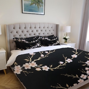 May include: Black duvet cover with a white and gold floral pattern. The duvet cover features a repeating pattern of delicate branches with pink blossoms. The duvet cover is shown on a bed with two matching pillowcases.