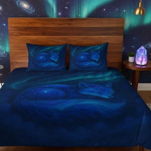 May include: A dark blue bedding set featuring a sleeping fox design. The set includes a duvet cover and two pillowcases. The fox is depicted in a starry night sky with shades of blue and teal. The bedding set is designed to fit a bed.