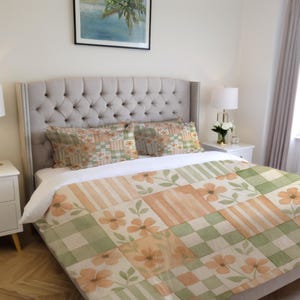 May include: A bed with a floral patterned comforter and pillow set. The comforter features a patchwork design with peach and green floral squares and stripes. The pillows have a similar floral pattern. The bed has a gray upholstered headboard.