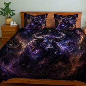 May include: A bedding set featuring a detailed illustration of a bull, the Taurus zodiac sign, set against a cosmic background of purple and gold. The set includes a comforter and two pillowcases, all with the same design.