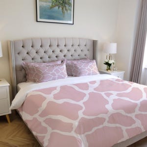 Puede incluir: Una funda nórdica de estampado de vaca rosa y blanca en una cama con cabecero capitoné. La cama tiene dos almohadas con un patrón geométrico.