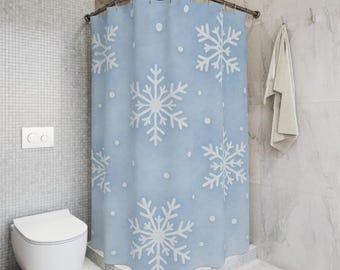Puede incluir: Una cortina de ducha azul claro con diseños de copos de nieve blancos grandes y puntos blancos más pequeños. La cortina está en una ducha de esquina, con un inodoro blanco y una toalla colgando en la pared.