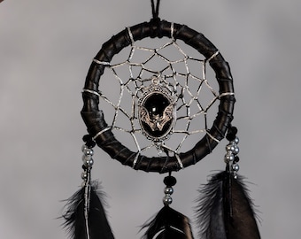 May include: A black dreamcatcher with a silver web design and black feathers. The center features a silver bat pendant on a black oval. The dreamcatcher is a decorative item.