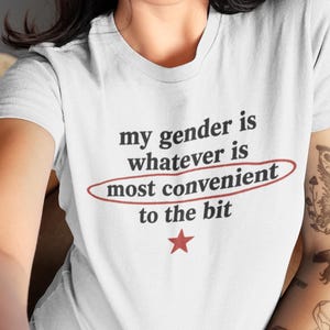 Può includere: Una t-shirt bianca a maniche corte con il testo nero "my gender is whatever is most convenient to the bit", con le parole "most convenient" cerchiate in rosso e una piccola stella rossa stampata sotto il testo sul davanti del capo.