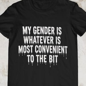 Pode incluir: Uma t-shirt preta de manga curta com texto branco que diz MY GENDER IS WHATEVER IS MOST CONVENIENT TO THE BIT. As letras têm um efeito de tinta a escorrer, criando um contraste marcante com o tecido preto sólido da peça de vestuário.