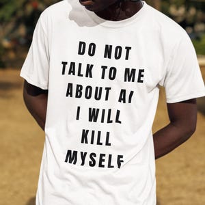Op de afbeelding: Een wit T-shirt met korte mouwen en vetgedrukte zwarte tekst op de voorkant met de tekst: DO NOT TALK TO ME ABOUT AI I WILL KILL MYSELF. Het shirt heeft een klassieke ronde hals en een standaard pasvorm, gemaakt van effen witte stof.