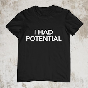 Puede incluir: Camiseta negra con el texto blanco "I HAD POTENTIAL" en el pecho. El texto está en negrita, sin serifa. La camiseta es de estilo cuello redondo clásico, hecha de un material suave.