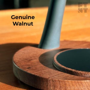 May include: Close-up of a wooden stand with a dark gray support and a black circular surface. The stand is made of genuine walnut and has a smooth, polished finish. The text "Genuine Walnut" is visible.
